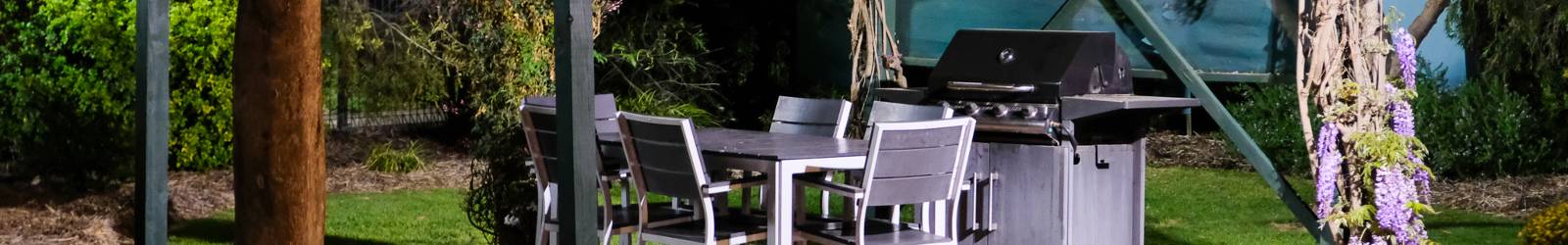 Outdoor barbecue and dining setting under pergola with native plants