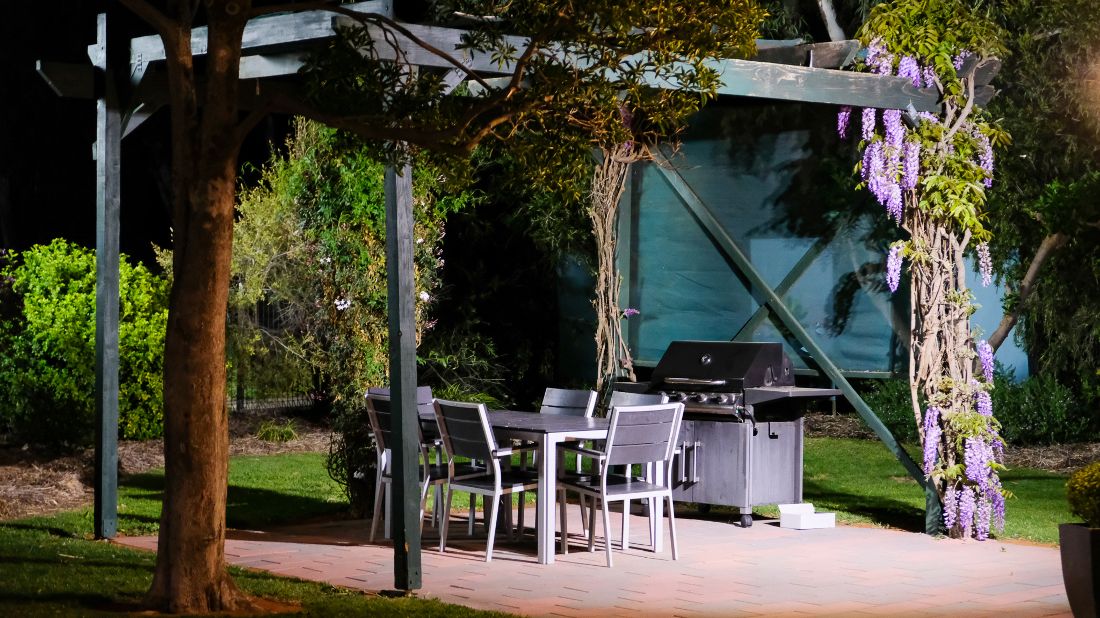 BBQ area under timber pergola with wisteria, outdoor furniture and lawn